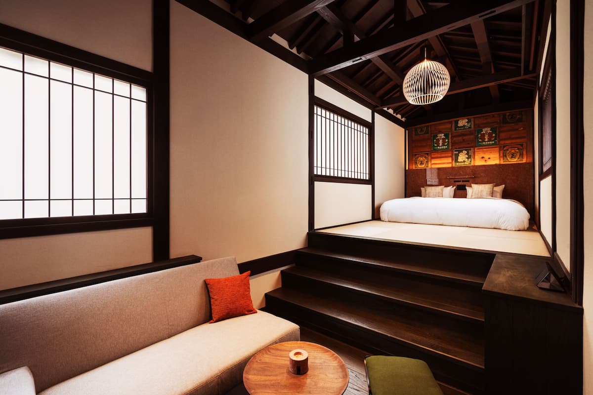 A traditional Japanese-style room with tatami flooring, a low wooden bed, a sofa, and a small table.