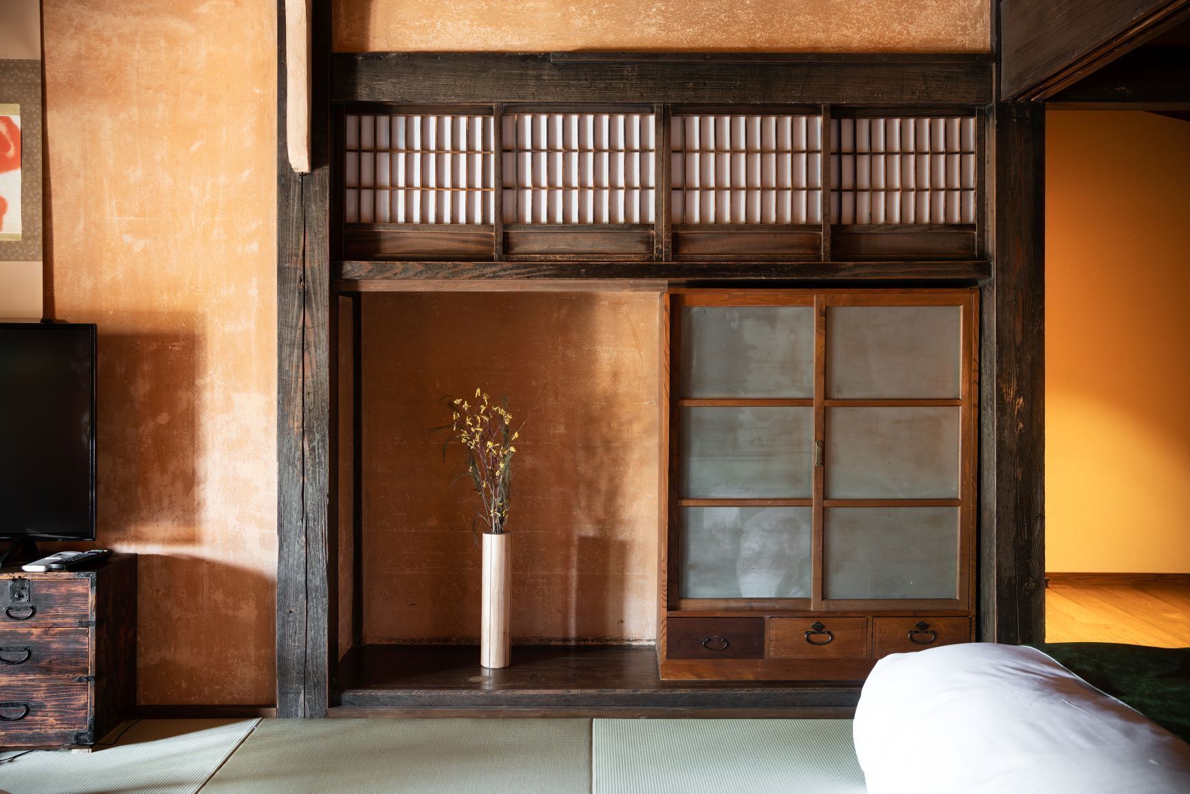 A traditional Japanese room with tatami flooring, a sliding door with a grid pattern, a wooden cabinet, and a vase with flowers.