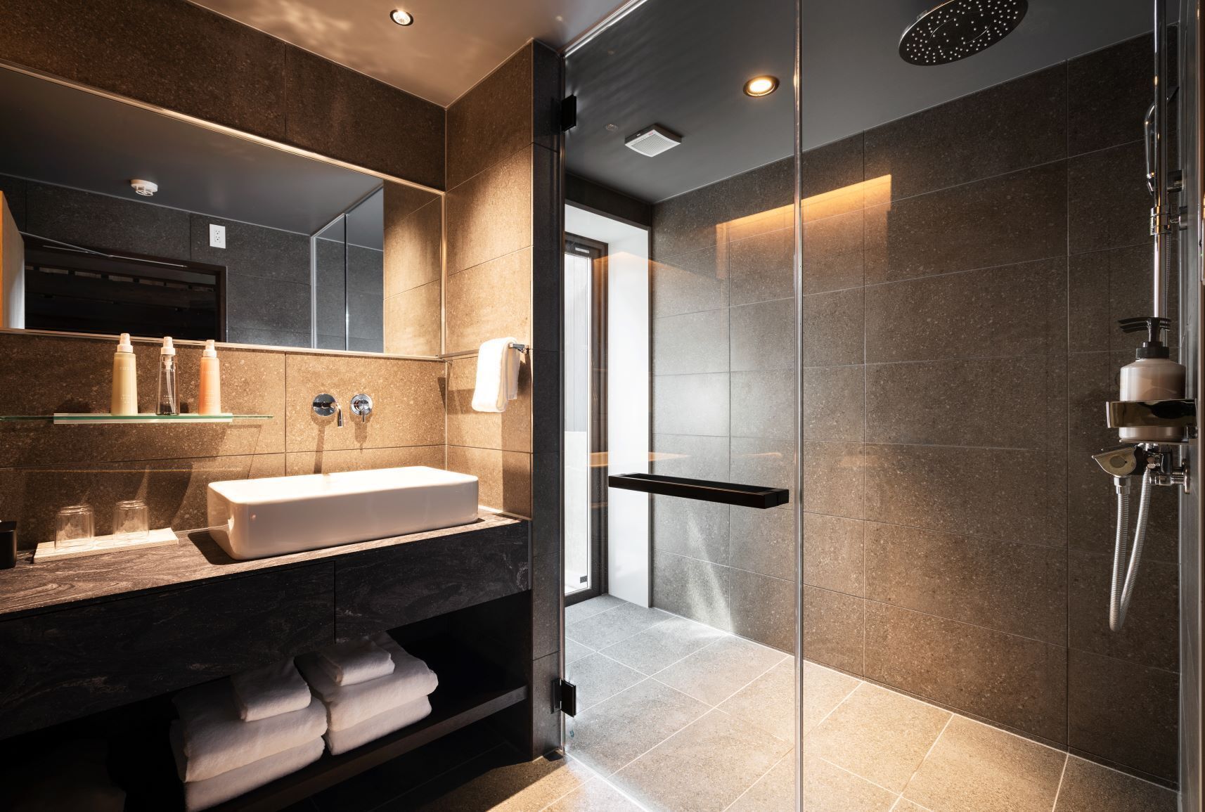 A modern bathroom with a glass shower enclosure, a large mirror, and a vanity with a sink and towel storage.
