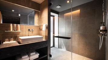 A modern bathroom with a glass shower enclosure, a large mirror, and a vanity with a sink and towel storage.