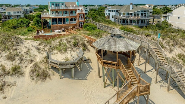 A beach house with a wooden deck, a gazebo, and a staircase leading to a second floor.