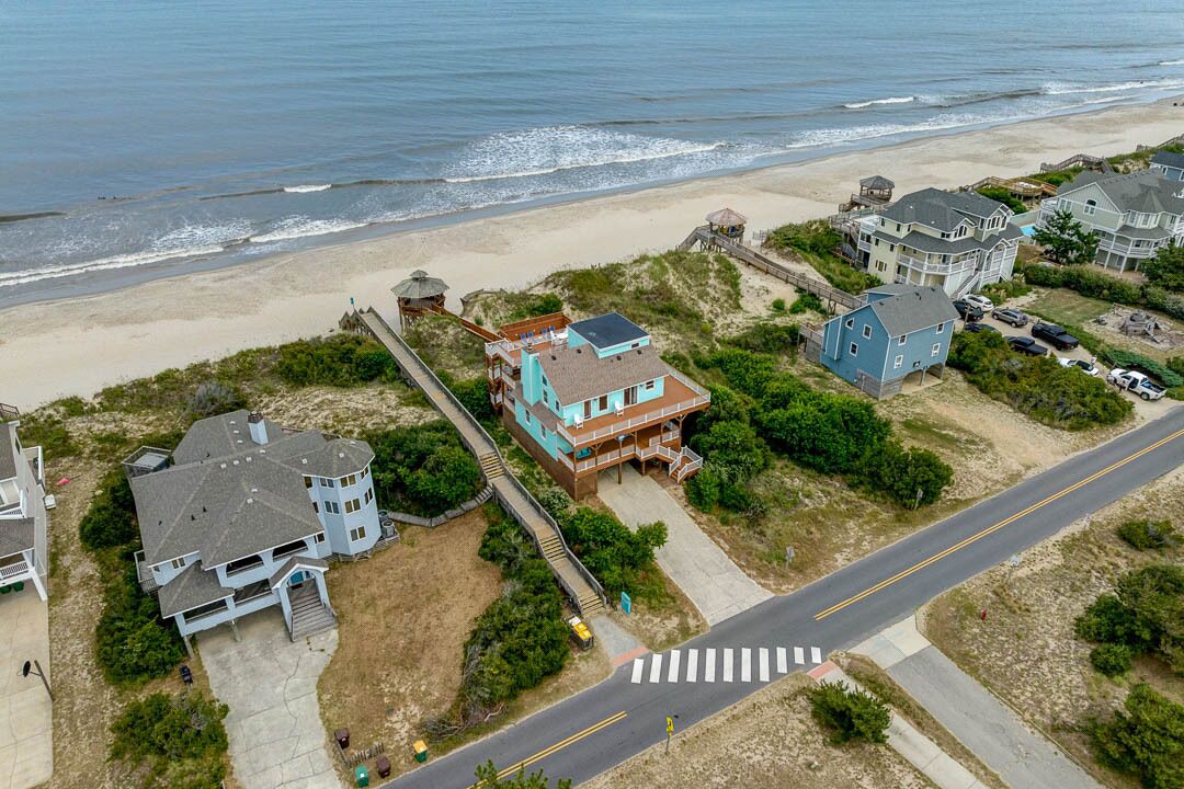 An aerial view of a coastal residential area with houses, a beach, and a road.