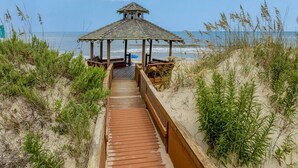 A wooden boardwalk leading to a gazebo with a view of the beach and ocean.
