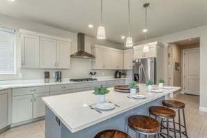 A modern kitchen with a central island, bar stools, stainless steel appliances, and pendant lighting.