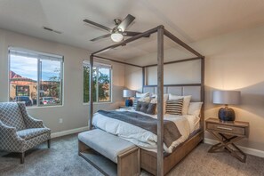 A four-poster bed with a canopy, bedside lamps, a chair, and a view of the outside.