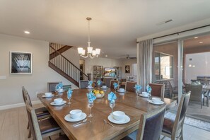 A dining area with a wooden table set for six, a chandelier, and a staircase leading to another level.