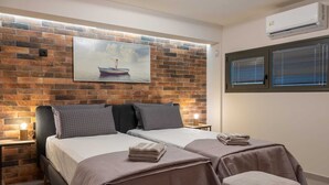A double room with two beds, a brick wall, a painting, an air conditioner, and a window with blinds.