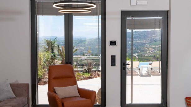 A modern living room with a leather armchair, a wooden coffee table, and a view of a pool and mountains through large glass doors.