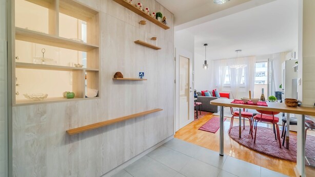A modern kitchen with wooden shelves, a dining area with red chairs, and a view to the living room. - Apartment Saga With Terrace And Parking (Zagreb)