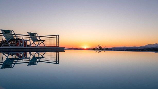 Un capvespre tranquil sobre un llac calmat, amb una terrassa que compta amb gandules i una barana.