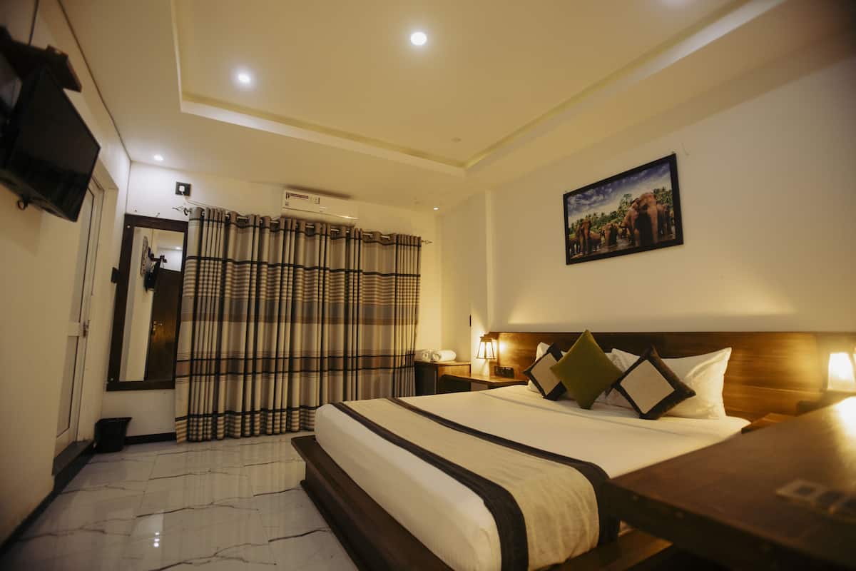 Quarto de hotel com uma cama grande, uma televisão de tela plana na parede, um quadro sobre a cama e uma cortina com padrão listrado.
