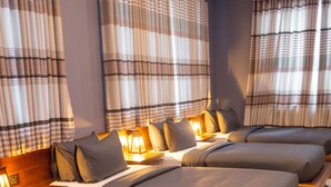 Ein Hotelzimmer mit vier nebeneinander stehenden Betten, jedes mit einem hölzernen Kopfteil und einem Nachttisch mit Lampe.