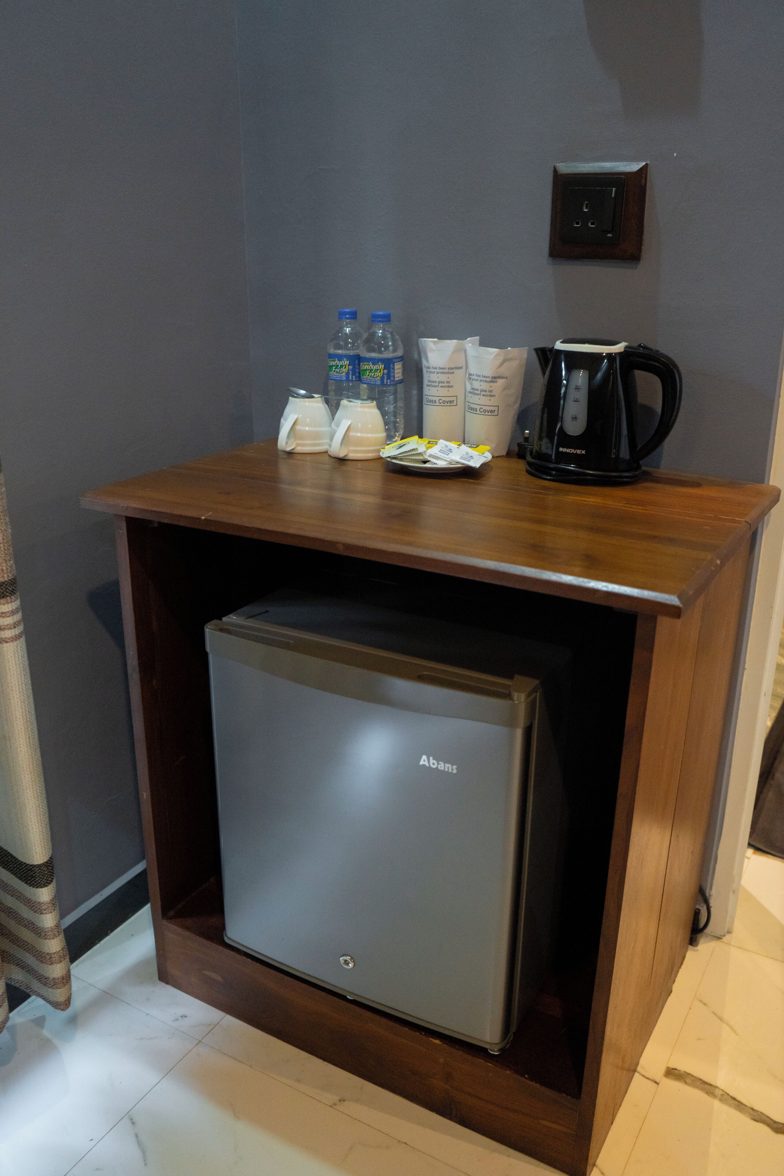 A compact minibar with a refrigerator, a coffee maker, bottled water, and coffee pods.
