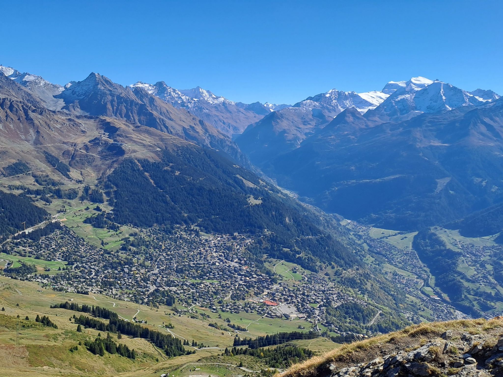 Un paisaje montañoso con un pueblo en el valle rodeado de zonas boscosas y picos nevados.