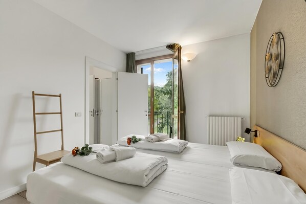 A hotel room with two beds, a wooden ladder, a radiator, and a view of greenery through a window.