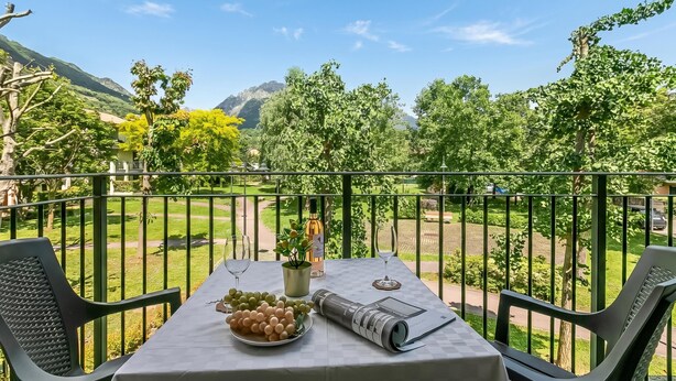Een balkon met een tafel gedekt voor twee personen, een fles, een plant en een schaal druiven.