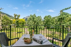 A balcony with a table set for two, a bottle, a plant, and a plate of grapes.