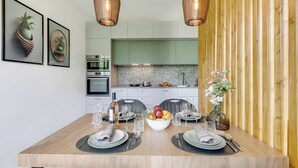 A dining area with a wooden table set for two, two framed pictures on the wall, a kitchen in the background, and a wooden partition. - Porto Letizia Roma 4, Porlezza, Italy (Porlezza)