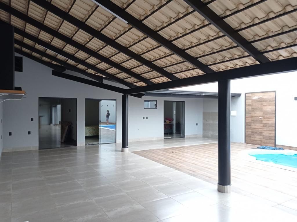 Uma sala de estar integrada com pé direito alto, piscina e deck de madeira.