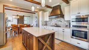 Une cuisine dotée de meubles en bois, d’un îlot central, d’appareils électroménagers en acier inoxydable et de luminaires suspendus.