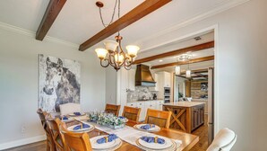 Un coin repas avec une table en bois dressée pour six personnes, un lustre et un grand tableau abstrait accroché au mur.