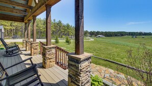 Une terrasse en bois avec des piliers en pierre, des sièges d’extérieur et une vue sur un champ verdoyant et des arbres.