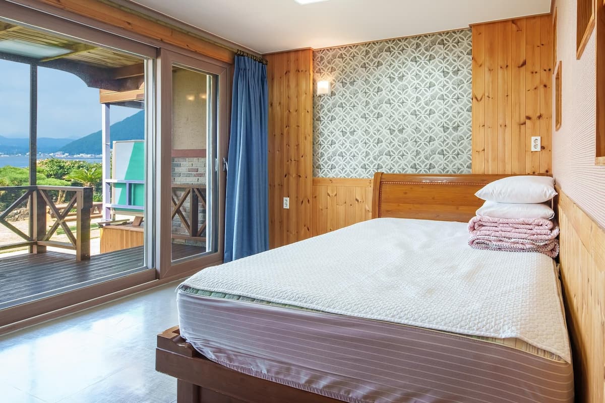 Une chambre avec un grand lit, une tête de lit en bois et une vue sur un balcon doté d’une balustrade en bois.