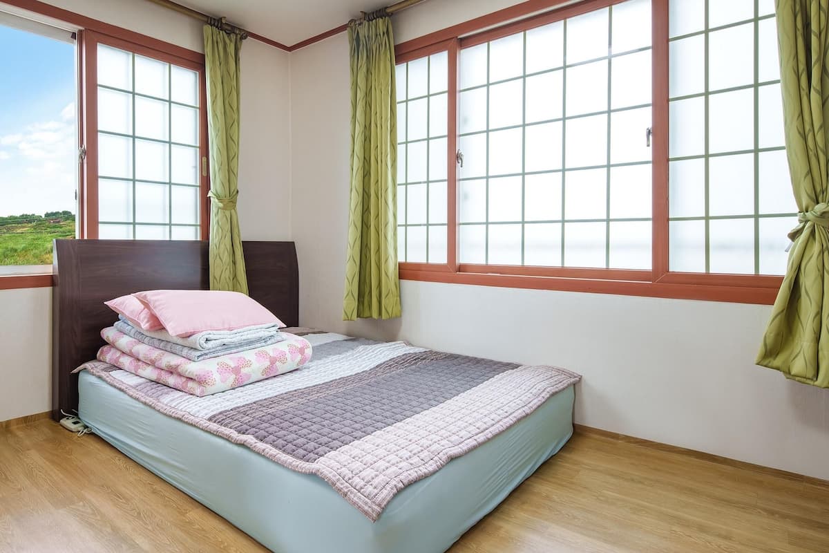 Une chambre à coucher avec un lit, des rideaux verts et une vue sur l’extérieur.