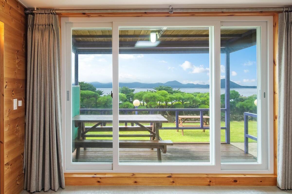Une pièce dotée d’une porte-fenêtre coulissante donnant sur une terrasse extérieure avec des tables de pique-nique, et offrant une vue sur un lac et des montagnes.