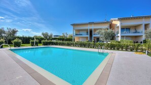 A rectangular swimming pool with a tiled deck, surrounded by a well-maintained hedge and a multi-story building with balconies. - Una Meta Tra Gli Ulivi - Pool and Private Terrace (Peschiera del Garda)
