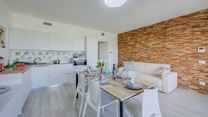 A modern kitchen with white cabinets, a wooden dining table set with plates, glasses, and a vase of flowers. - Una Meta Tra Gli Ulivi - Pool and Private Terrace (Peschiera del Garda)