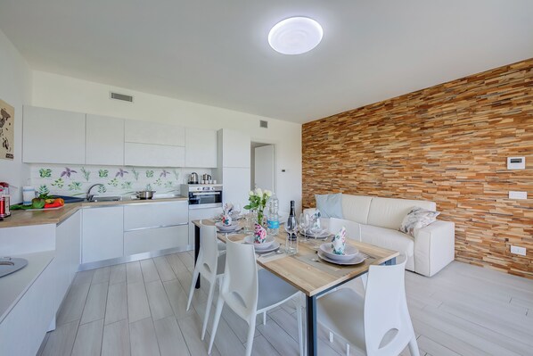 A modern kitchen with white cabinets, a wooden dining table set with plates, glasses, and a vase of flowers.