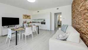 A modern living room with a flat-screen TV, dining table, and white furniture. - Una Meta Tra Gli Ulivi - Pool and Private Terrace (Peschiera del Garda)