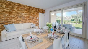 A modern living room with a wooden accent wall, a white sofa, and a dining area set for four with a view of the outdoors. - Una Meta Tra Gli Ulivi - Pool and Private Terrace (Peschiera del Garda)