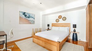 A modern bedroom with a wooden bed, two bedside tables with lamps, a desk, and a chair.