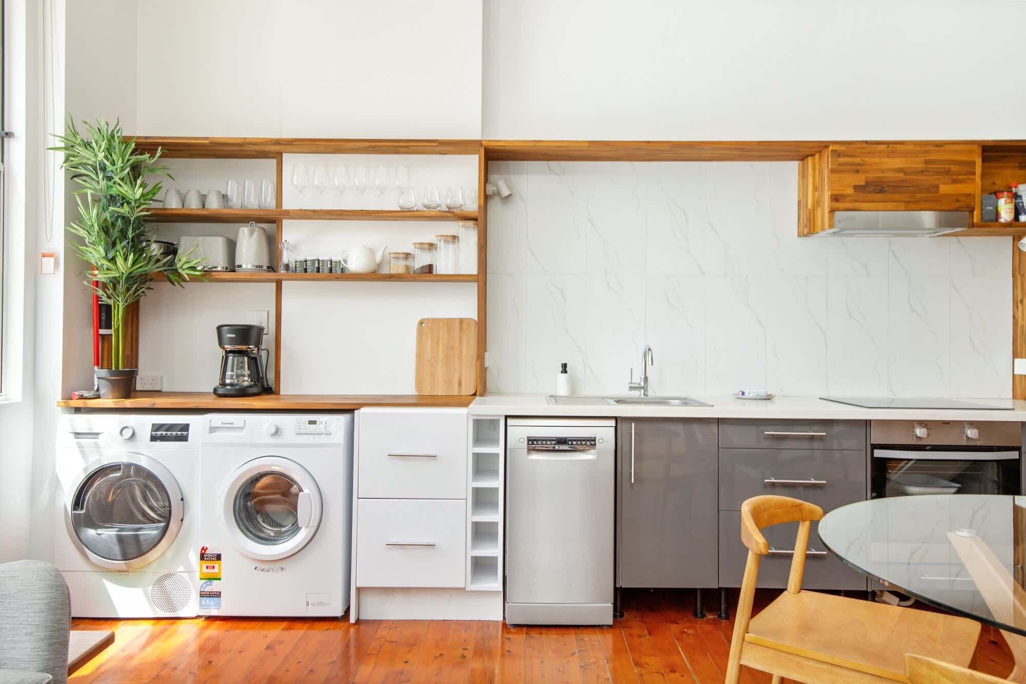 A compact kitchen with a washing machine, dishwasher, and a dining area with a table and chair.