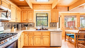 Una cocina con armarios de madera, estufa, lavavajillas y un comedor con sillas y una mesa.