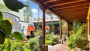 Un patio techado con un horno de ladrillo, plantas en macetas y una pérgola.