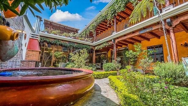 Un patio con una gran fuente, abundante follaje y un edificio con varios balcones y zonas de estar al aire libre.