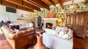 Un salón acogedor con pared de piedra, chimenea, sofás de cuero y suelo de baldosas.