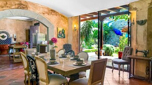 Un comedor con una mesa dispuesta para cuatro personas, rodeada de sillas, un refrigerador y una zona de cocina al fondo.