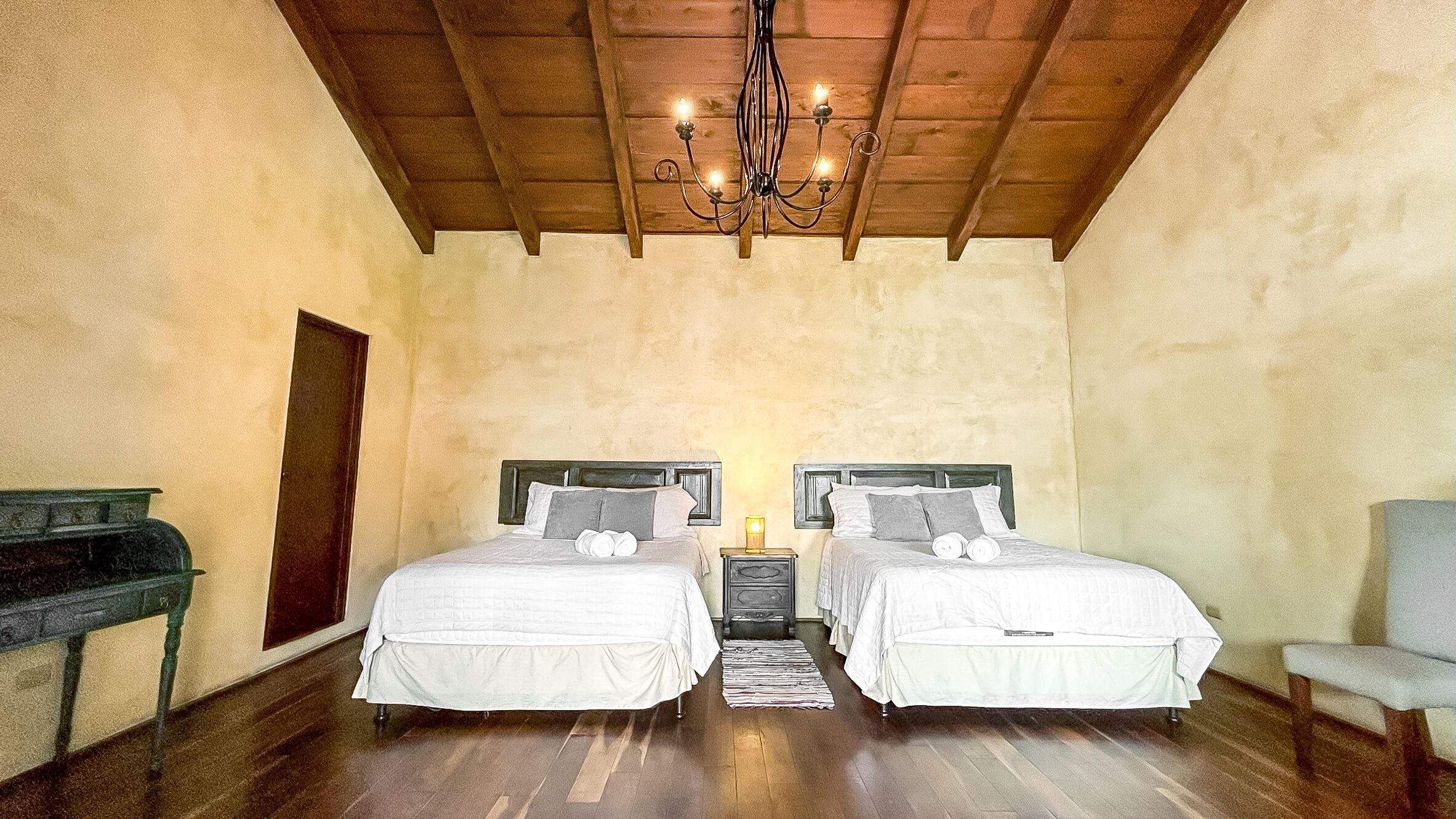 A bedroom with two beds, wooden floors, a chandelier, and a piano.