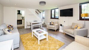 Ein modernes Wohnzimmer mit Sofa, Sessel, Couchtisch und einem an der Wand montierten Fernseher.