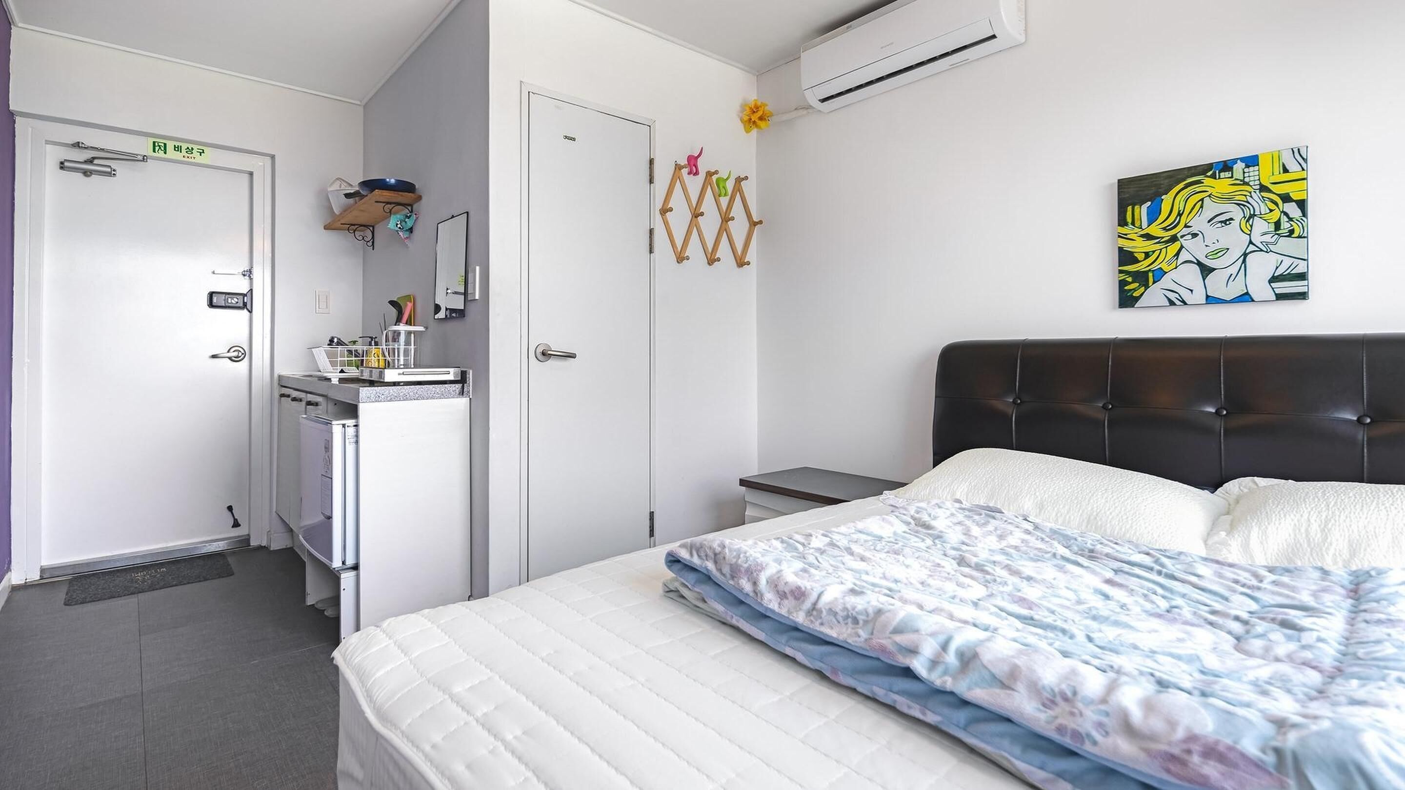 A hotel room with a bed, a small desk, a wardrobe, and an air conditioning unit.
