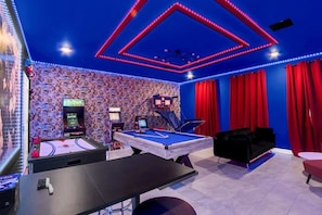 A room with a pool table, a dartboard, and arcade games.