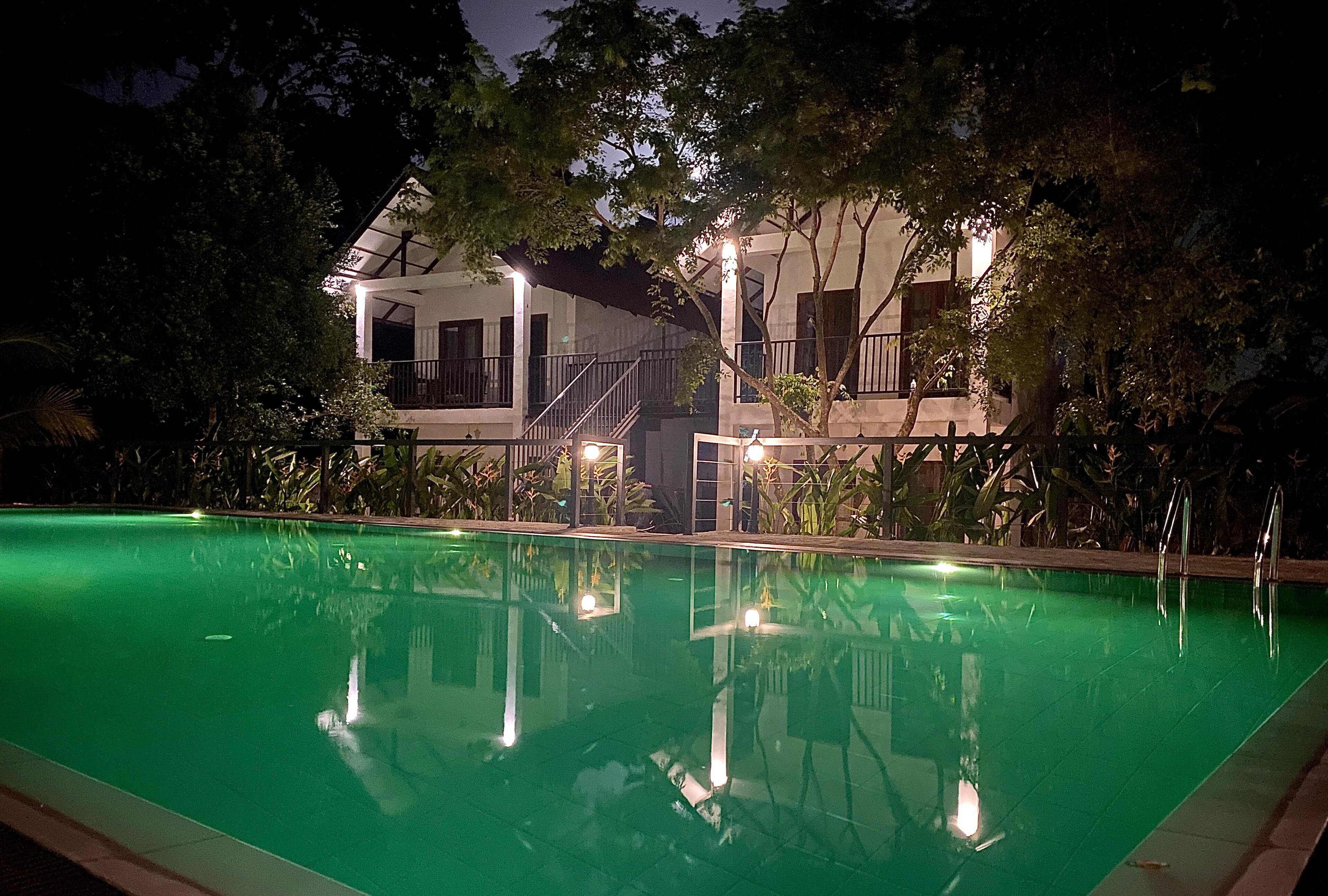 Una piscina con una casa al fondo, rodeada de árboles.