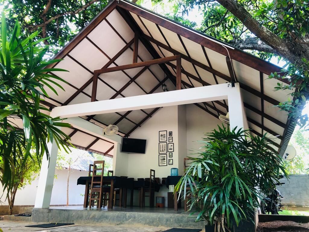 A covered outdoor area with a dining table and chairs, surrounded by potted plants.
