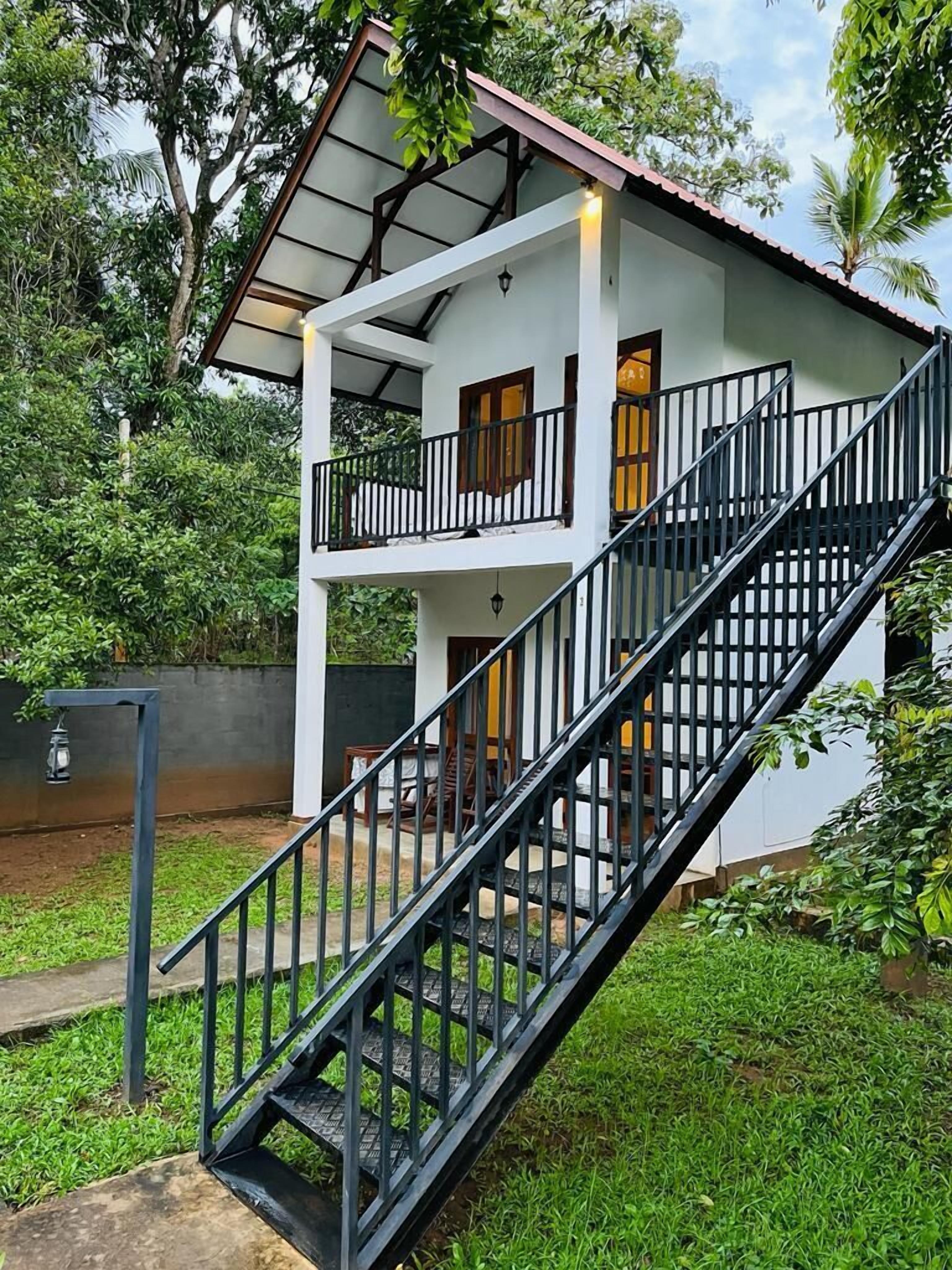 Un edificio de dos pisos con balcón, escaleras y un pequeño jardín.