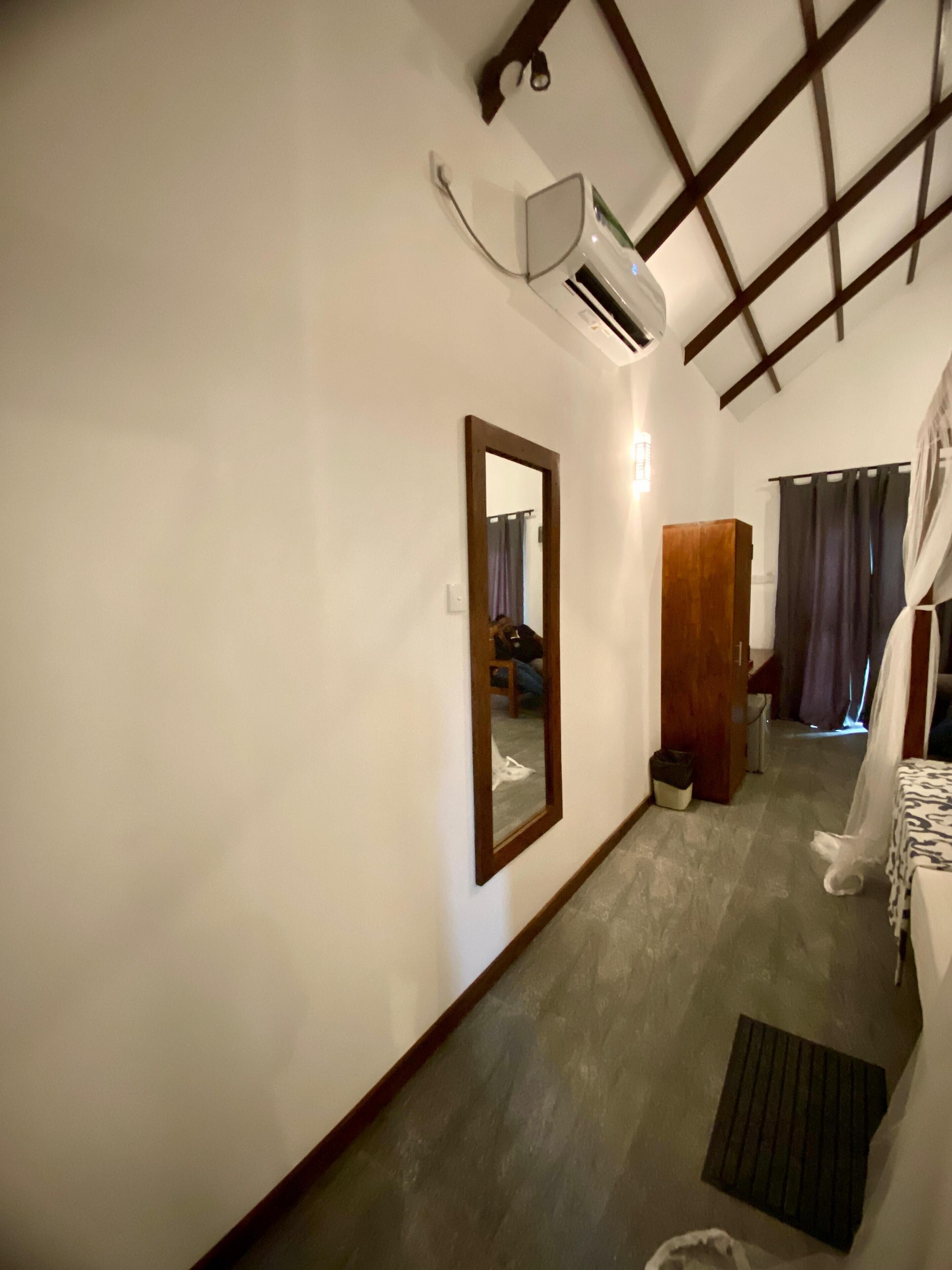 A bedroom with a bed, a mirror, an air conditioning unit, a window with curtains, and a small rug.