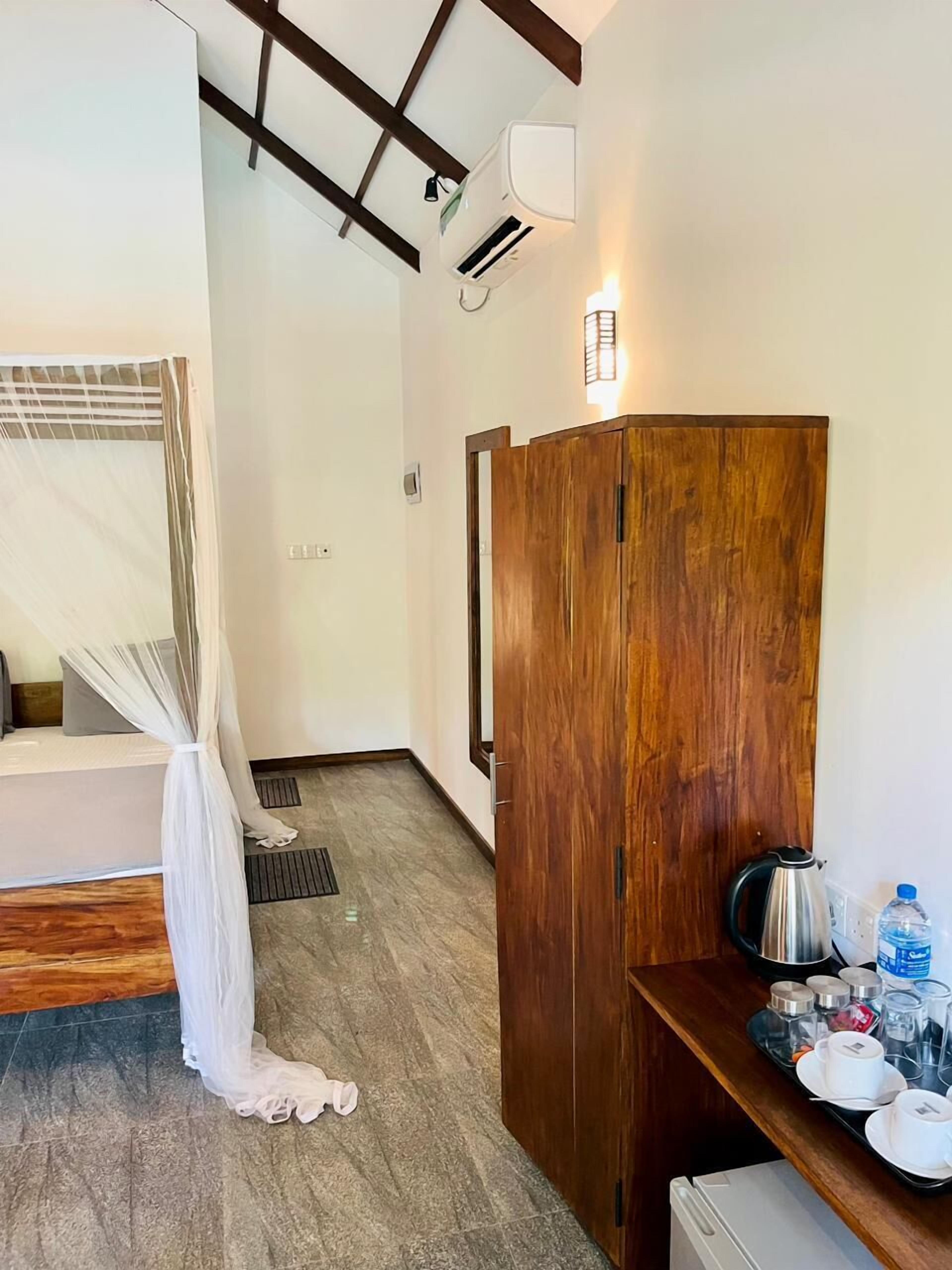 Une chambre d’hôtel avec un lit, une armoire en bois, une petite kitchenette et un ventilateur de plafond.